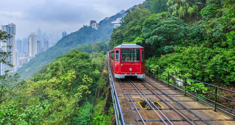 El icónico Peak Tram rojo asciende por vías montañosas exuberantes con vistas al horizonte de Hong Kong envuelto en neblina.
