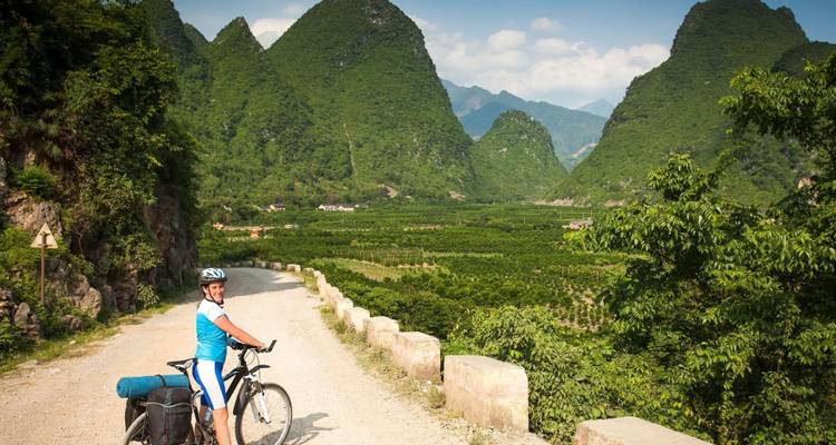El ciclista se detiene en un camino de tierra rodeado de picos de karst espectaculares y valles verdes.