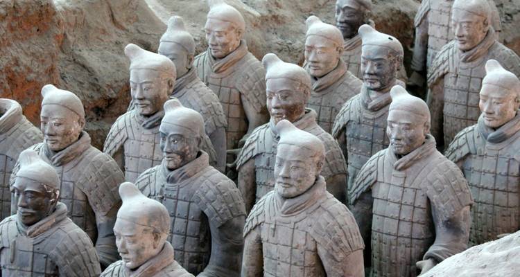 Filas de guerreros de terracota de piedra se encuentran de pie en fosas excavadas, cada uno con características faciales distintas.