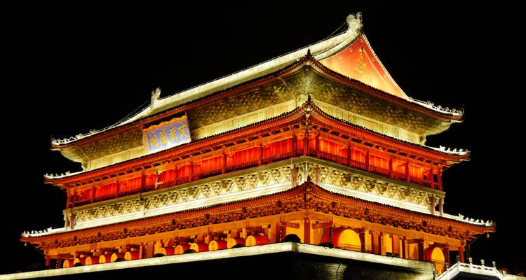La Torre del Tambor de Xi'an iluminada en rojo y oro vívidos contra el cielo nocturno.