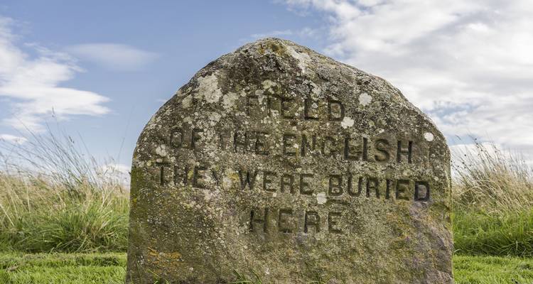 Stone marker with engraved text, set in a grassy field.