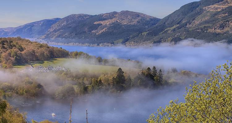 Vallée brumeuse avec des collines luxuriantes et un lac.
