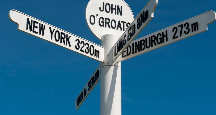 Señalización direccional blanca en John O'Groats mostrando las distancias a ciudades alrededor del mundo contra un cielo azul.