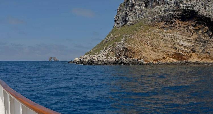 Vue depuis un bateau d'une île rocheuse escarpée s'avançant dans les eaux bleu profond du Pacifique sous un ciel légèrement nuageux.