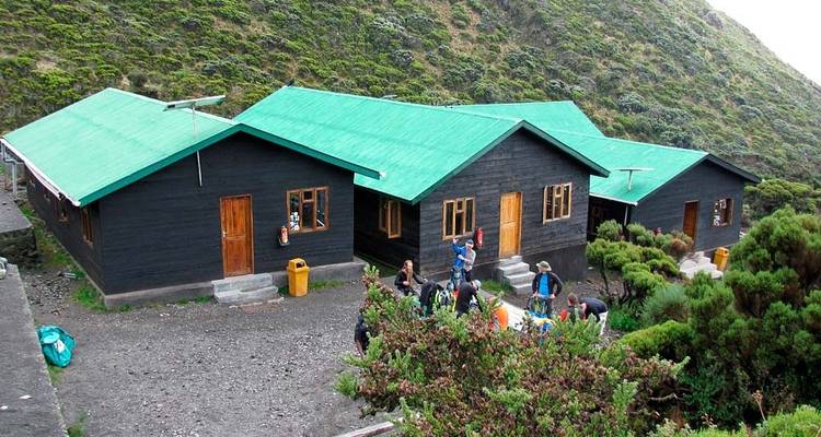 Gruppe von Wanderern vor Berghütten an einem bewaldeten Hang.