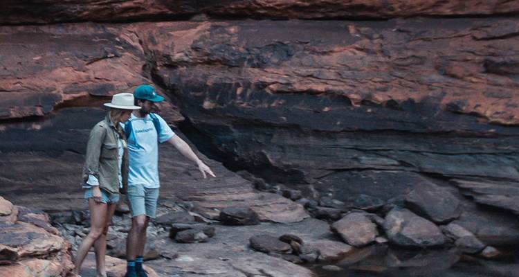 Excursionistas examinando escarpadas paredes naranjas del cañón con rocas dispersas y charcos.