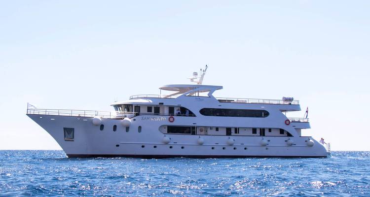 Moderno crucero blanco pequeño anclado en el mar azul tranquilo bajo un cielo brillante