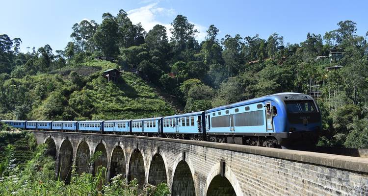 Zug, der die berühmte Neun-Bogen-Brücke überquert, umgeben von üppigem Grün.