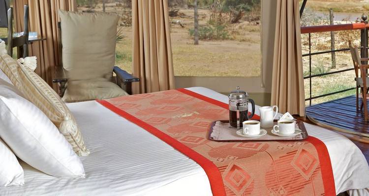 Comfortable safari tent bedroom with neatly prepared coffee service overlooking dry bushland.