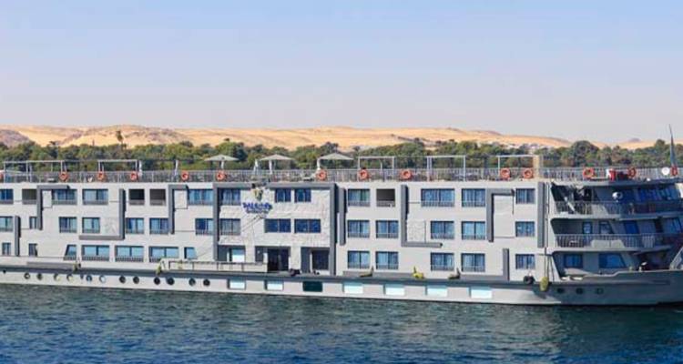 Modernes Nilkreuzfahrtschiff, das auf ruhigem blauen Wasser mit Wüstenhügeln im Hintergrund segelt.