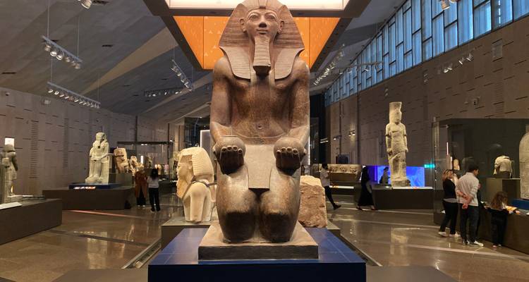 Statue d'un pharaon égyptien assis dans un musée avec des visiteurs.