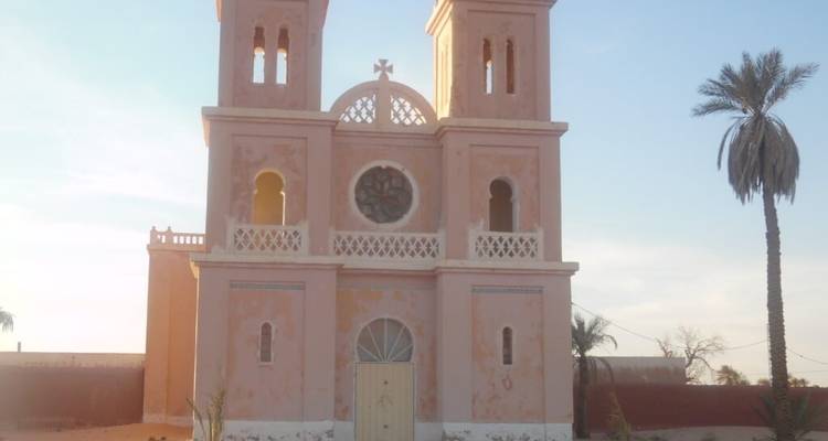 Un bâtiment d'église rose dans une zone désertique avec un seul palmier.