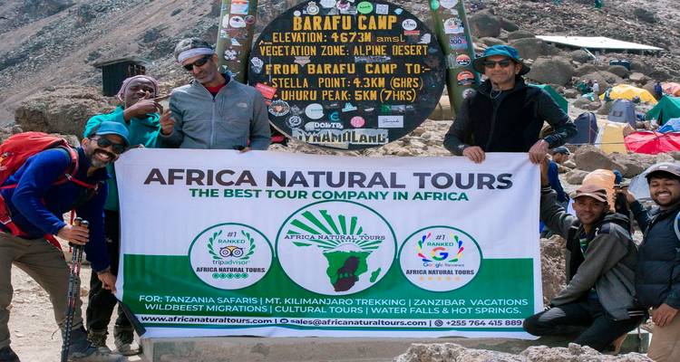 Group with a banner at Barafu Camp, mountain setting.