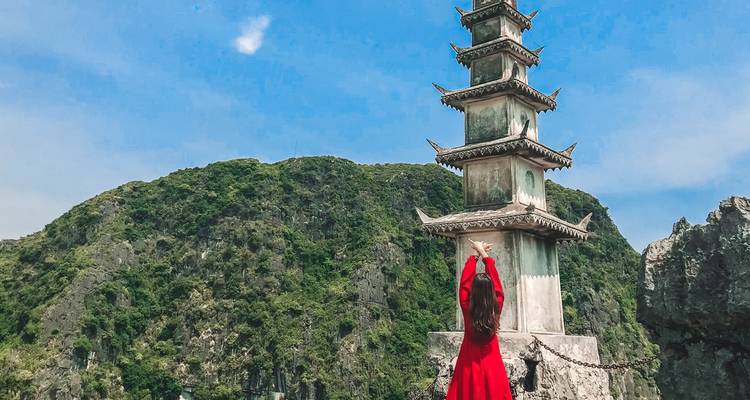 Person raising arms in front of a tall pagoda with a mountain backdrop.