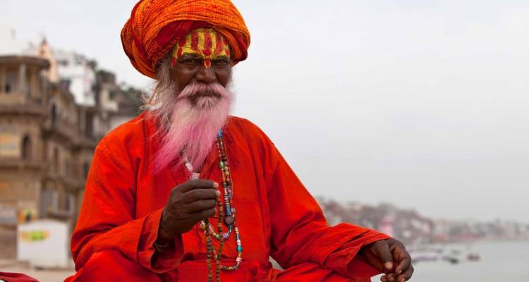 Un homme âgé en tenue traditionnelle indienne assis à l'extérieur avec un arrière-plan urbain flou.