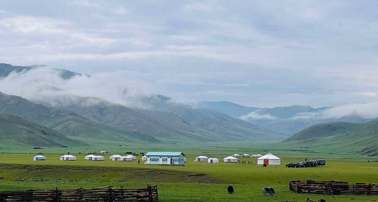 Large vallée verte parsemée de yourtes blanches et de chaînes de montagnes brumeuses sous un ciel nuageux.