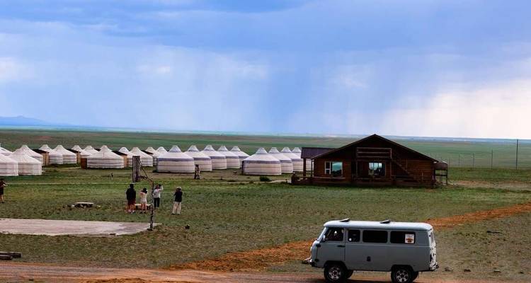 Rangée de yourtes dans la steppe avec des voyageurs et un van soviétique classique sous un ciel menaçant.