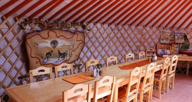 Intérieur d'une salle à manger spacieuse en yourte avec des tables en bois et des murs en treillis.