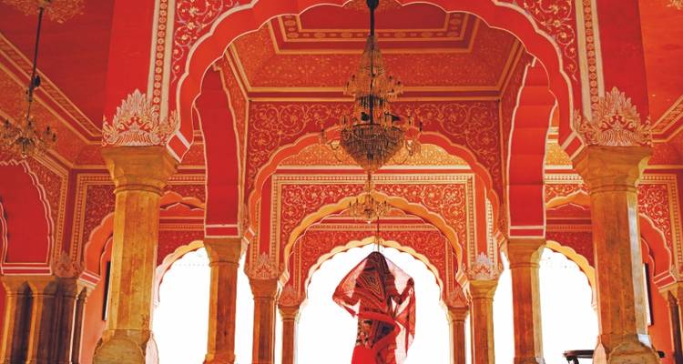 Mujer con sari rojo caminando bajo los arcos rosas ornamentados de un palacio indio