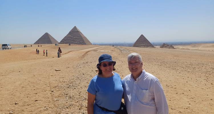 Pareja posando frente a las pirámides de Giza bajo un cielo azul despejado.
