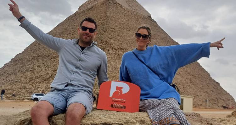 Pareja posando frente a una pirámide con un letrero de tour.