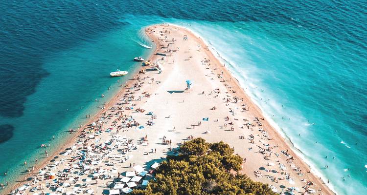 Vue panoramique de la langue de sable doré de Zlatni Rat remplie de baigneurs et entourée par une mer turquoise.