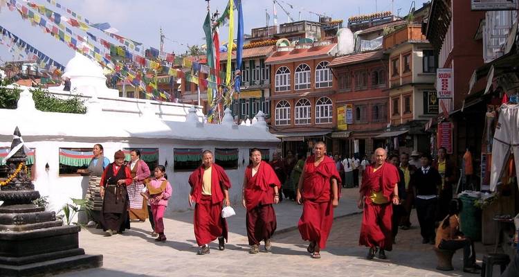 Des moines marchant dans une rue avec des bâtiments traditionnels.