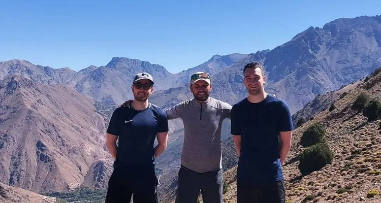 Tres amigos posando juntos frente a un fondo montañoso.