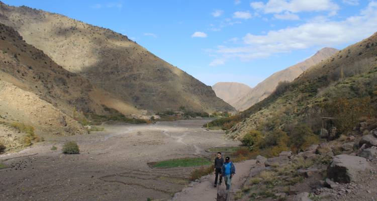 Pareja caminando por un valle con montañas de fondo bajo un cielo despejado.