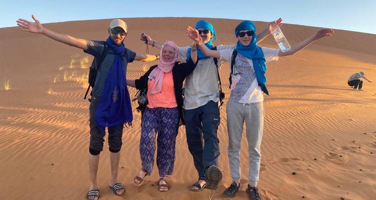 Grupo de amigos con vestimenta desértica posando en una duna de arena.
