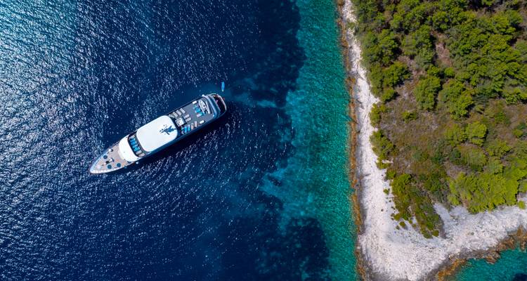Vue aérienne d'un yacht ancré près d'un littoral boisé.