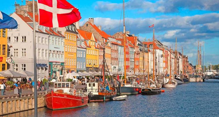 Coloridas casas urbanas del siglo XVII de Nyhavn, Copenhague, con viejos barcos de vela en el frente y una gran bandera danesa ondeando.