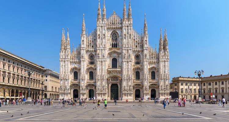 Grande façade du Duomo gothique de Milan dominant la vaste piazza grouillante de visiteurs et de pigeons.