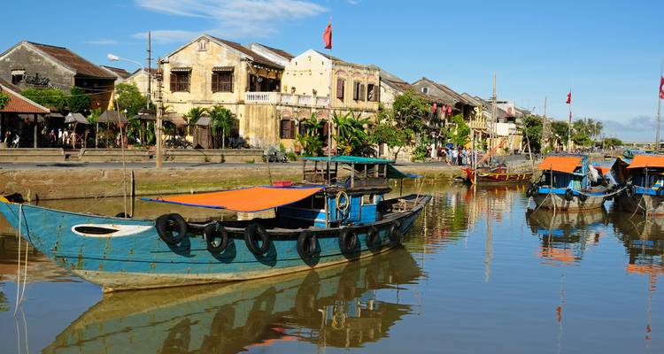 Colorful riverside houses and moored fishing boats reflect in calm water in Hoi An Ancient Town.