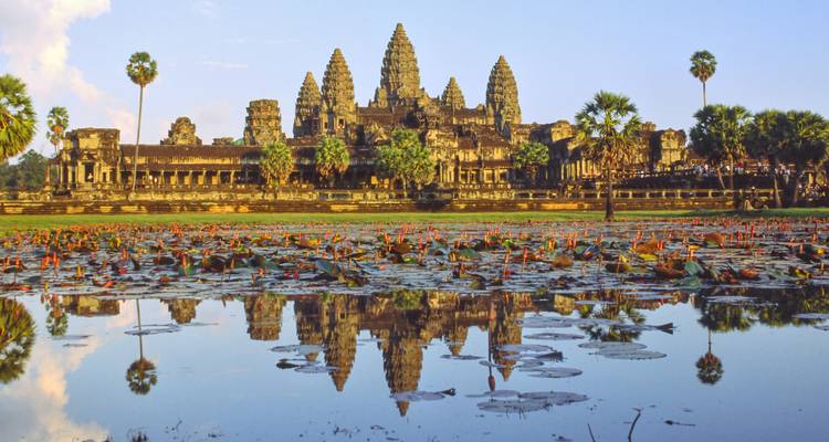 Iconic towers of Angkor Wat mirrored perfectly in a lotus-filled reflecting pool at dawn.