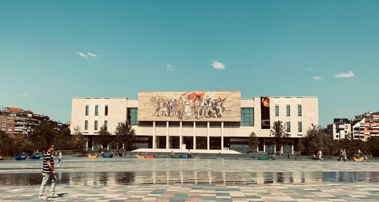 Grand bâtiment avec une œuvre d'art en mosaïque sur la façade dans une place de la ville.