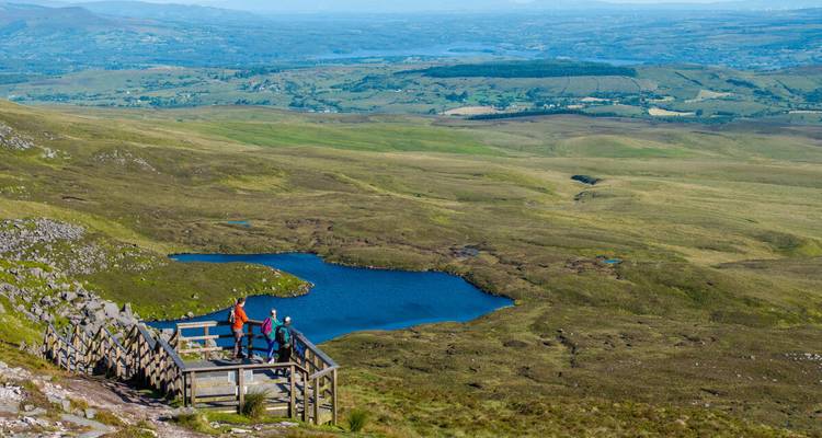 Trois personnes debout sur une plateforme en bois surplombant un paysage pittoresque.