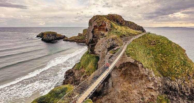 Pont suspendu au-dessus de falaises escarpées menant à une île rocheuse.