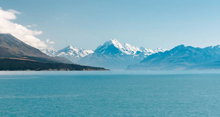 Un lago azul tranquilo se extiende hacia picos cubiertos de nieve bajo un cielo despejado.