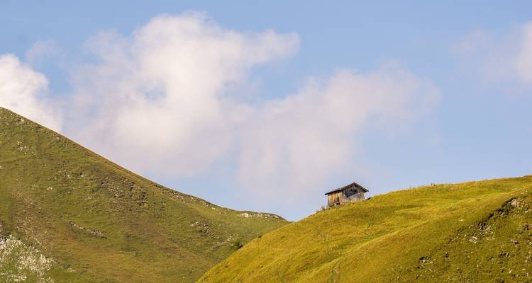 Small cabin on a grassy hill with a blue sky.