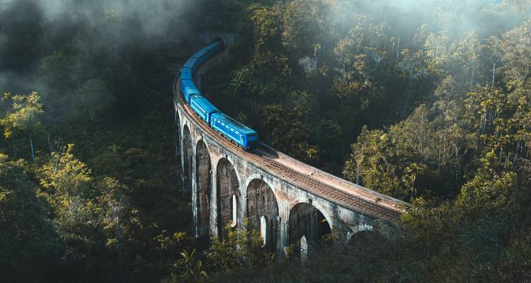 Le train bleu traverse l'emblématique pont à neuf arches du Sri Lanka au milieu d'une jungle luxuriante enveloppée de brouillard.