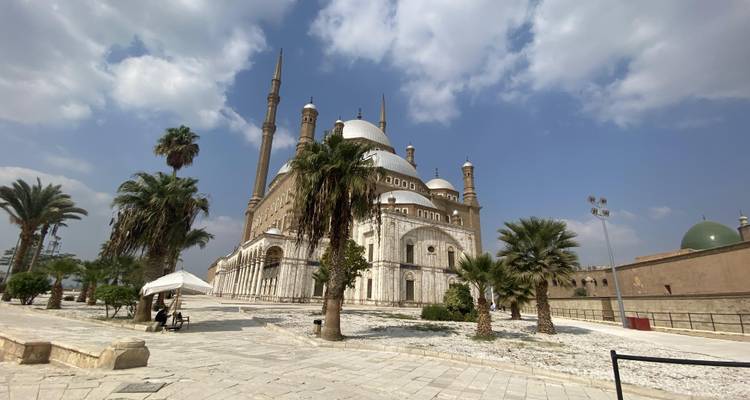 A beautiful mosque with minarets and palm trees under a bright sky.