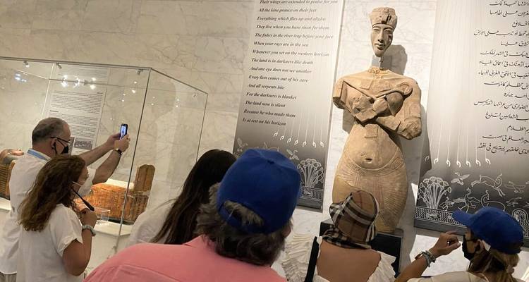 Visitors observing a statue inside a museum with inscriptions on the wall.