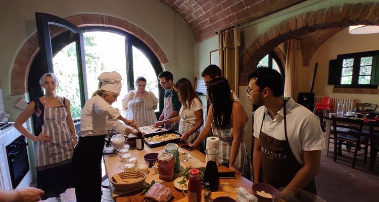 Los participantes de la clase de cocina se reúnen alrededor de una isla de cocina toscana rústica mientras el chef demuestra un plato.