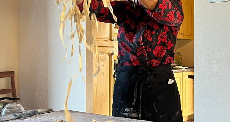 El cocinero lanza tiras de masa de pasta fresca bien alto sobre una superficie de trabajo de madera.