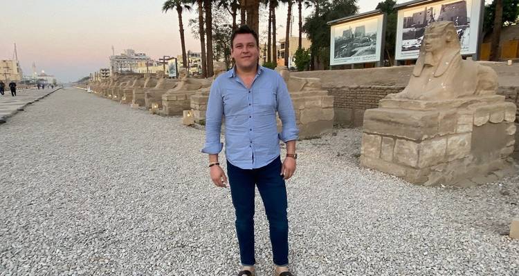 Hombre parado junto a estatuas de esfinges a lo largo de una avenida.