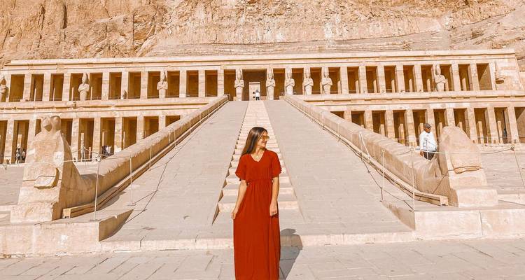 Une personne en robe rouge debout devant un temple égyptien antique.