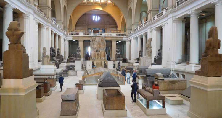 Interieur van een grote hal in een museum met verschillende Egyptische artefacten en een paar bezoekers.
