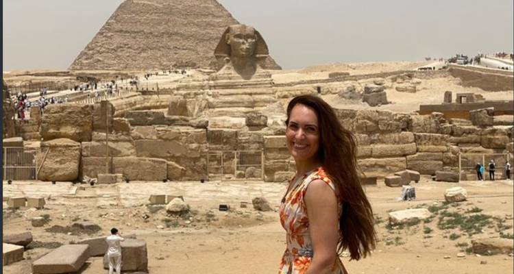 Woman smiles with the Great Sphinx and Pyramid of Khafre towering in the hazy desert behind.