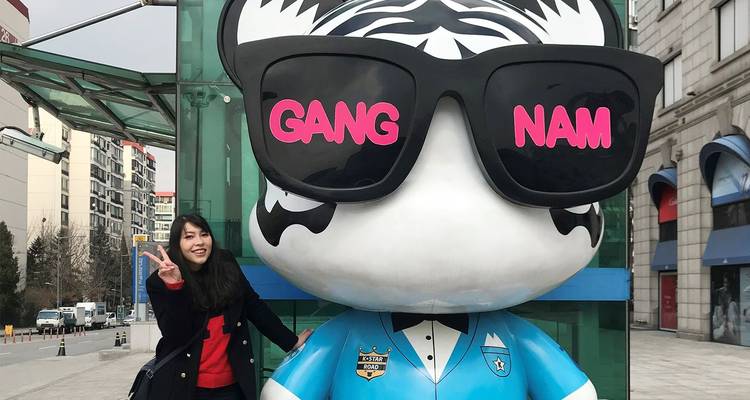 Mujer posando con señal de paz junto a una estatua gigante de panda usando gafas de sol con el texto 'GANG NAM'.